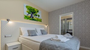 A modern bedroom with a bed, bedside tables, a nightstand, a large mirror, and a wall-mounted painting of a tree. - Villa Loki- your exclusive Holiday Home in Istria (Lašići, Vizinada)