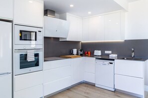 A modern kitchen with white cabinetry, a built-in oven, a microwave, a coffee maker, and a dishwasher.