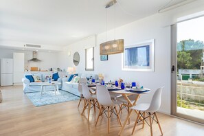 A modern living room with a dining area, a kitchen in the background, and a large window providing a view.