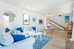 A modern living room with a sofa, coffee table, and a dining area with chairs and a table.