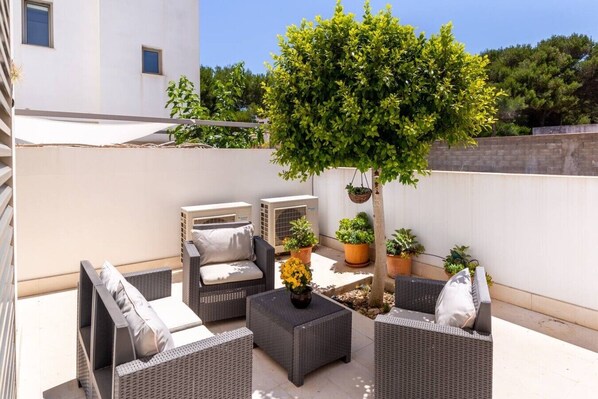 An outdoor patio area with wicker furniture, a tree, and potted plants.