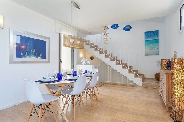 A dining area with a staircase leading to another level, white walls, and a blue seascape painting.