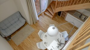 Un comedor con una mesa redonda, sillas blancas y una araña. Se observa una escalera con barandillas de madera que conduce a un nivel superior.