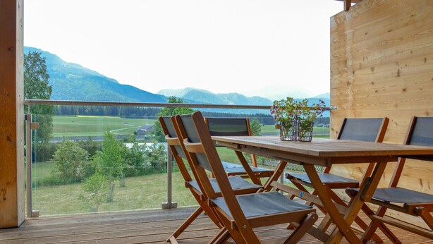 Una terraza de madera con una mesa y sillas, con vistas a un paisaje montañoso.
