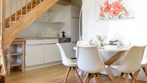 Una cocina moderna con armarios blancos, una escalera de madera y un comedor con sillas y una mesa blancos.