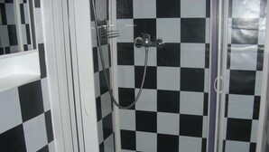 A bathroom with a checkered black and white tile wall, a shower with a handheld showerhead, and a sink with a faucet. - Small apartment central location Fulda Rhön Vogelsberg Hesse 2 pers. (Künzell)