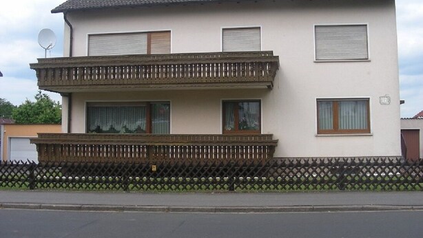 A two-story residential building with a balcony, a satellite dish, and a fenced yard. - Small apartment central location Fulda Rhön Vogelsberg Hesse 2 pers. (Künzell)