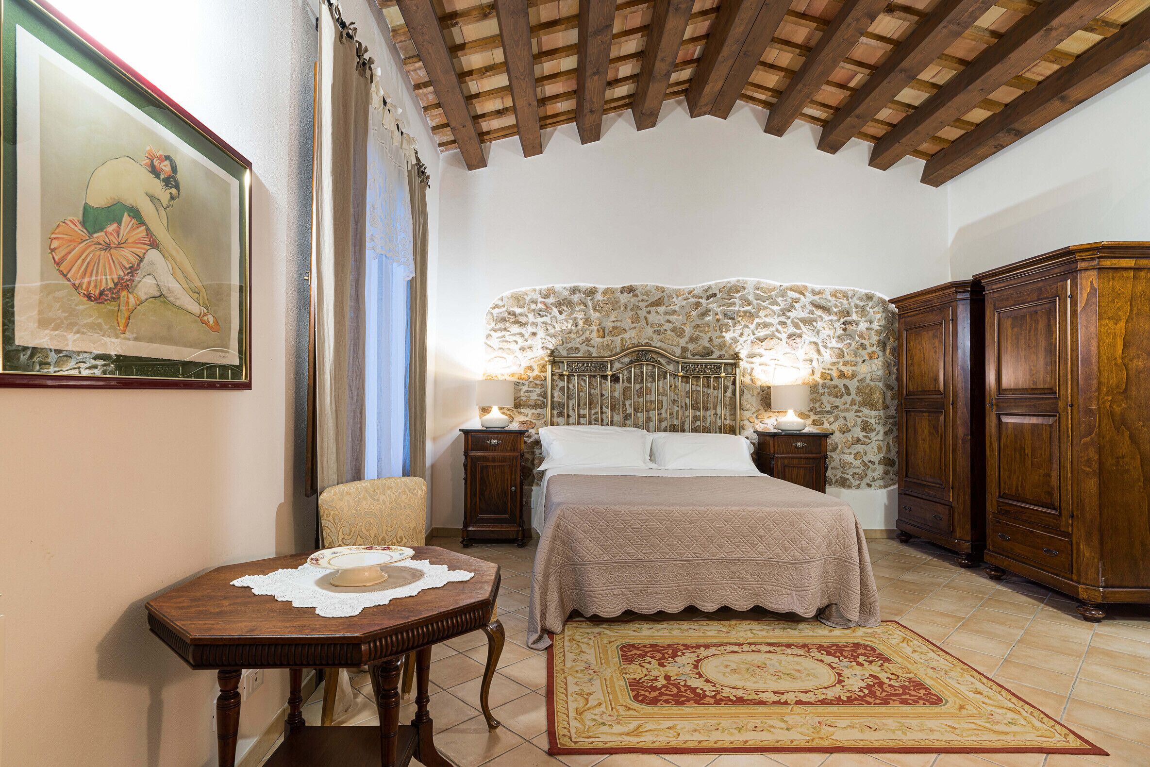 A bedroom with a stone headboard, wooden furniture, a bed with a beige bedspread, a small table with a doily, and a patterned rug.