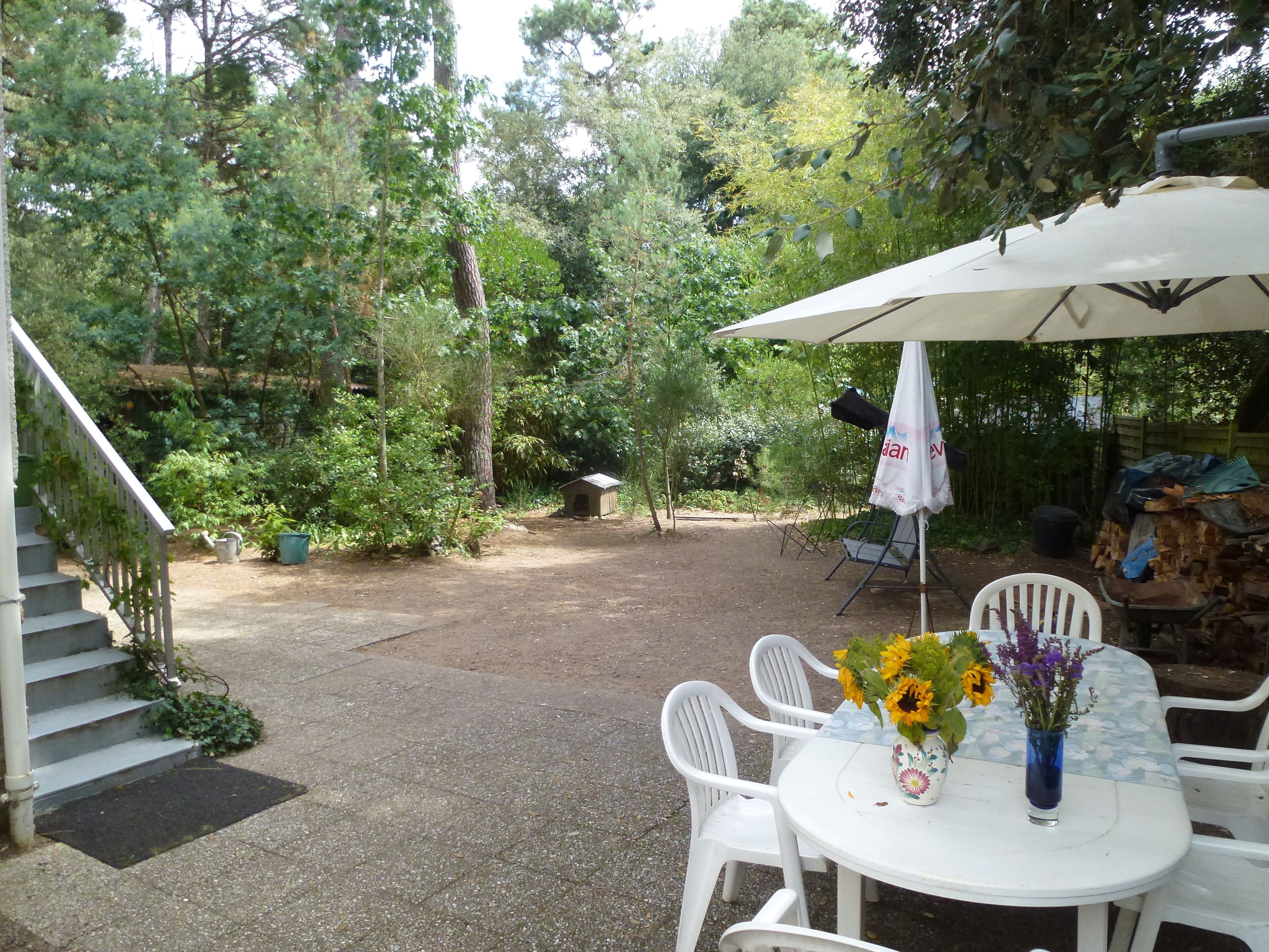 Un patio con una mesa y sillas blancas, una zona de estar cubierta y una caseta pequeña para perros.