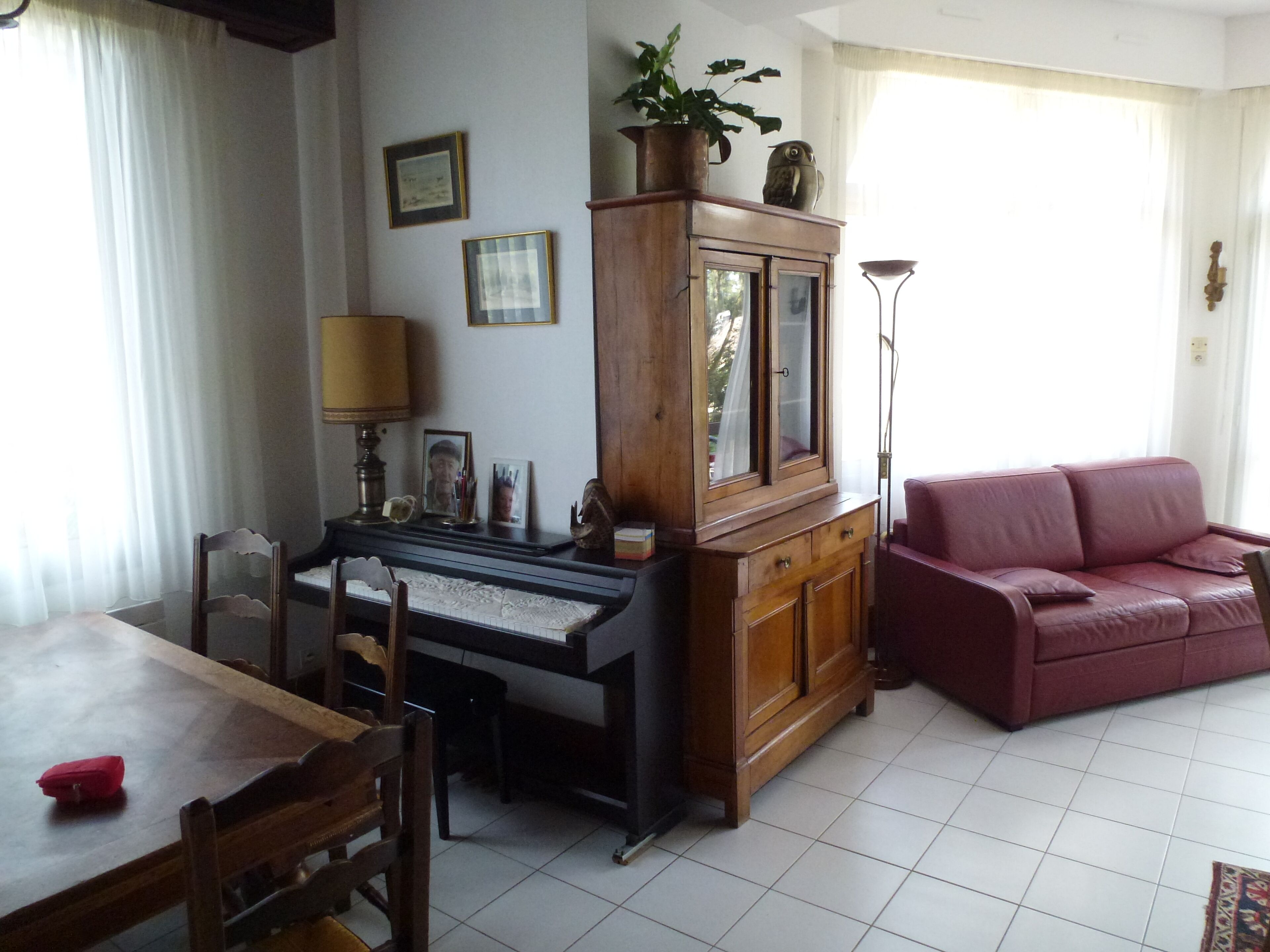 Una sala de estar con un piano, un sofá rojo, un aparador de madera y una lámpara.