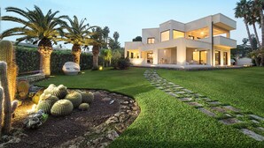 Une maison moderne à deux étages, dotée d’une pelouse bien entretenue, de palmiers et de cactus.