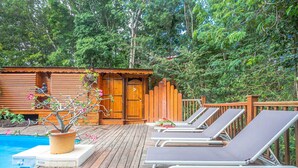 Eine Holzterrasse mit Pool, Liegestühlen und einer kleinen Holzhütte mit Tür.