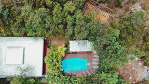 Eine Luftaufnahme einer Anlage mit einem Swimmingpool, umgeben von dichtem Grün, einer überdachten Terrasse und zwei geparkten Autos in der Nähe des Pools.