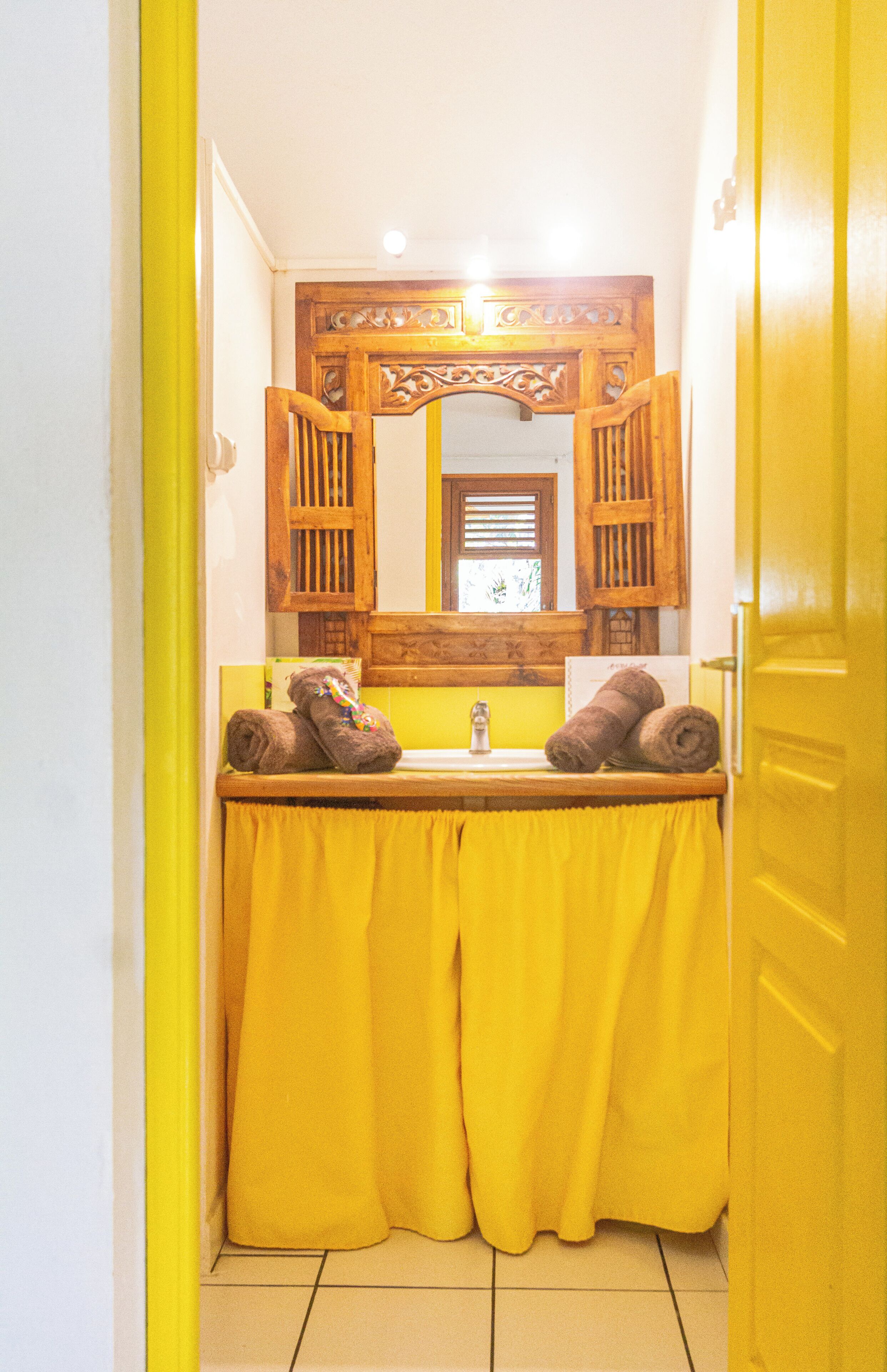 A bathroom with a yellow sink, wooden vanity, and a mirror with a decorative frame.