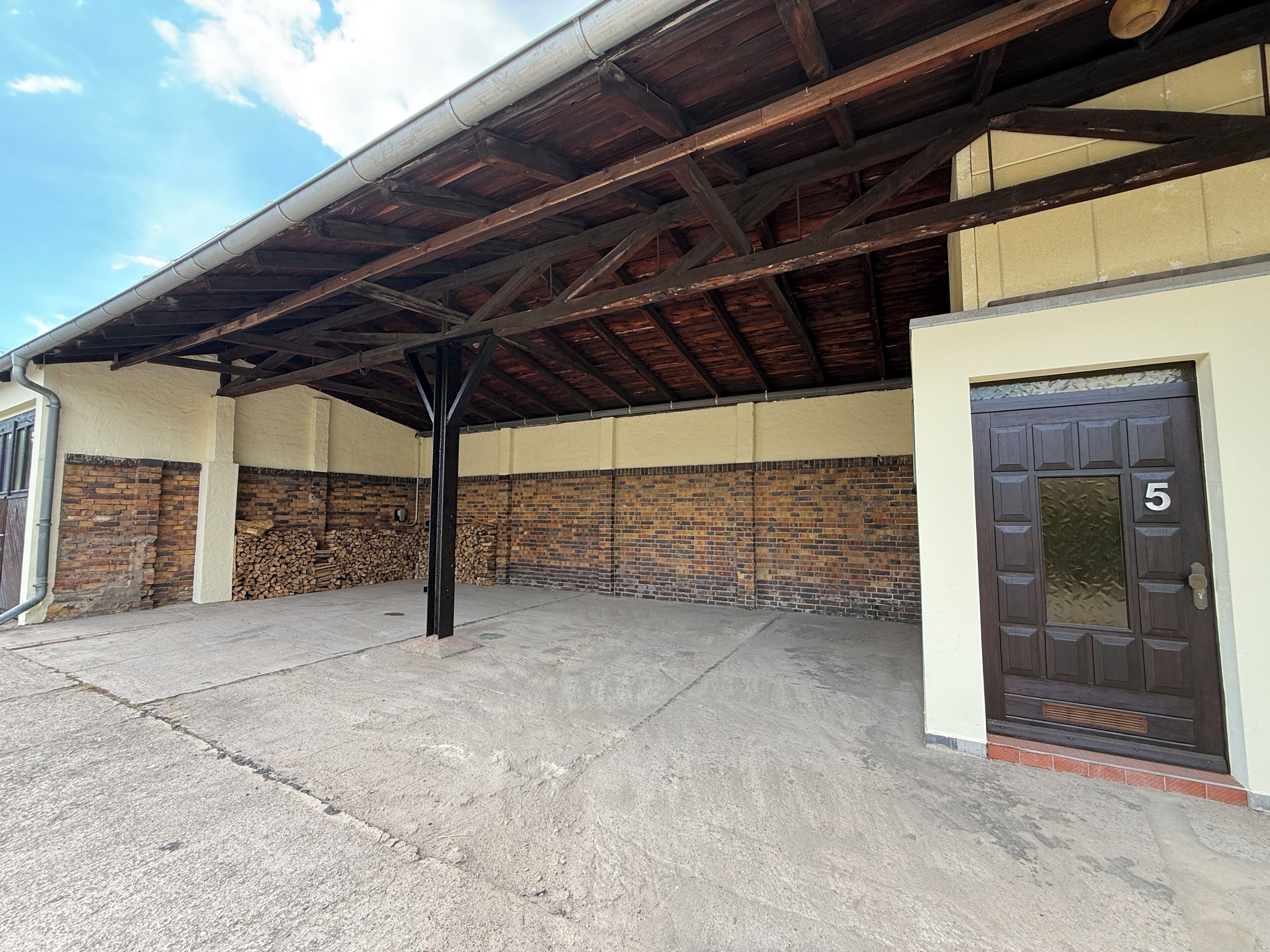 A covered outdoor area with a brick wall, a concrete floor, and a door marked with the number 5.