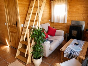 Een gezellig houten interieur van een chalet, met een bank, een potplant, een open haard en een houten ladder.