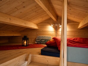 Een gezellig slaapkamer op zolder met houten balken, een oude camper, een lantaarn en een rode deken.
