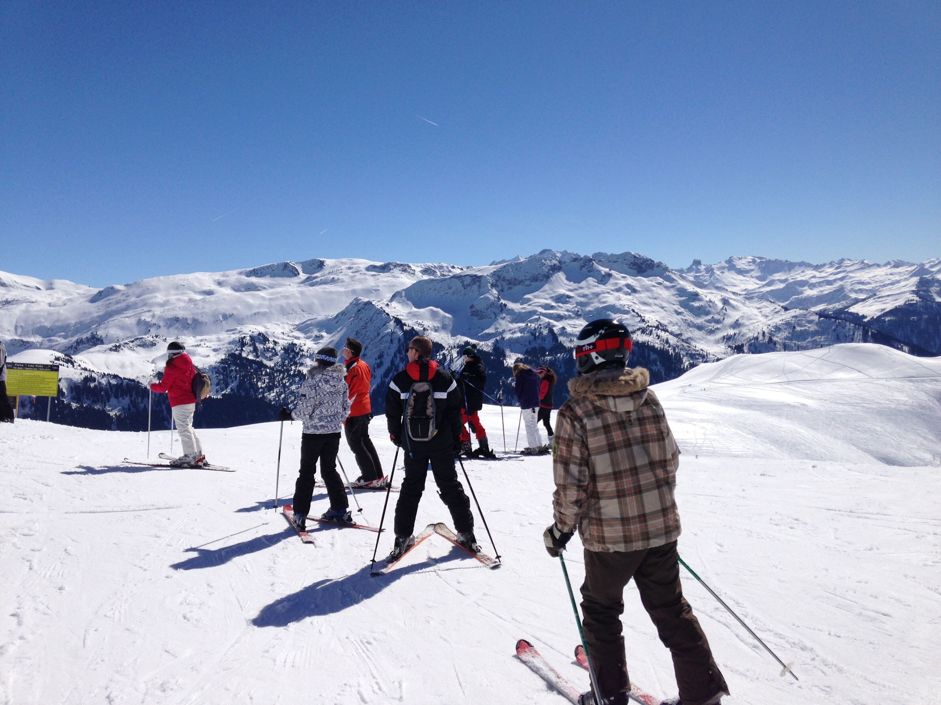 A group of skiers on a snowy slope with mountains in the background.