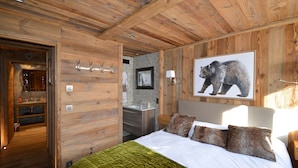 A wooden-paneled bedroom with a bed, a bathroom, and a hallway.
