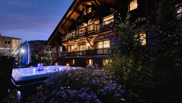 A wooden chalet with a hot tub and a balcony overlooking a garden with flowers.