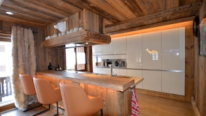 A modern kitchen with wooden accents, a bar area with bar stools, and a large window with curtains.