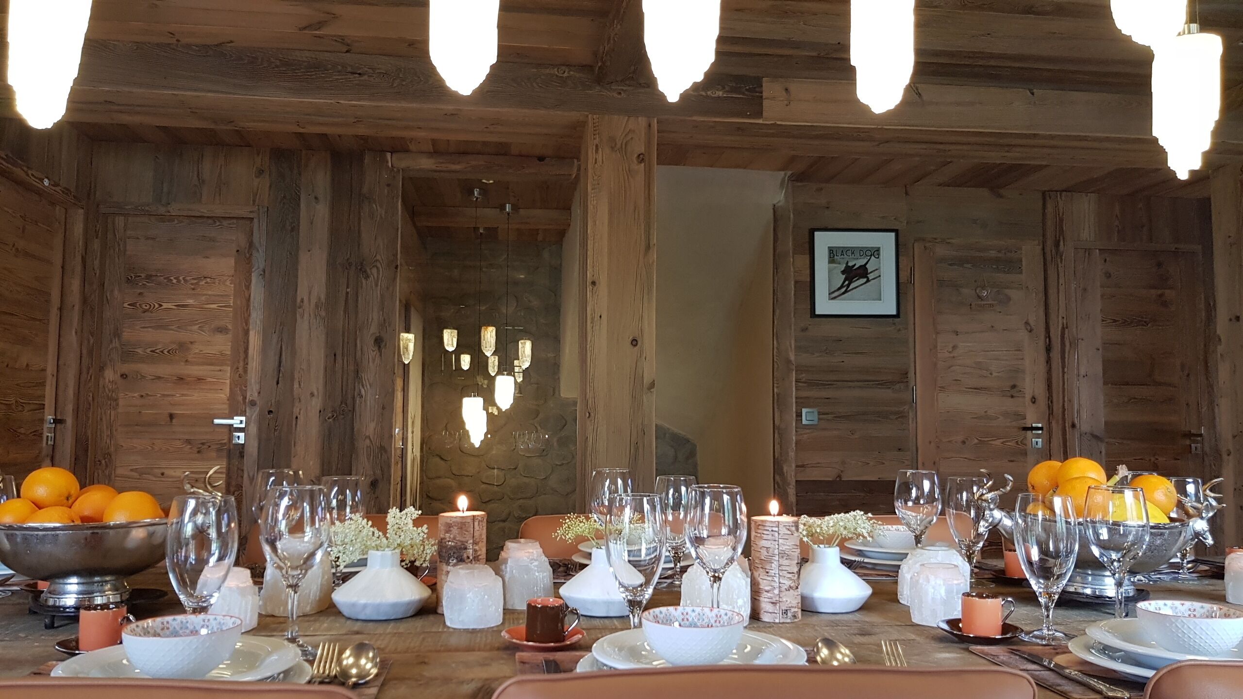 A wooden dining table set with glassware, candles, and oranges.