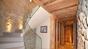 A staircase with stone walls and wooden beams, leading to a hallway with wooden flooring and a stone wall.