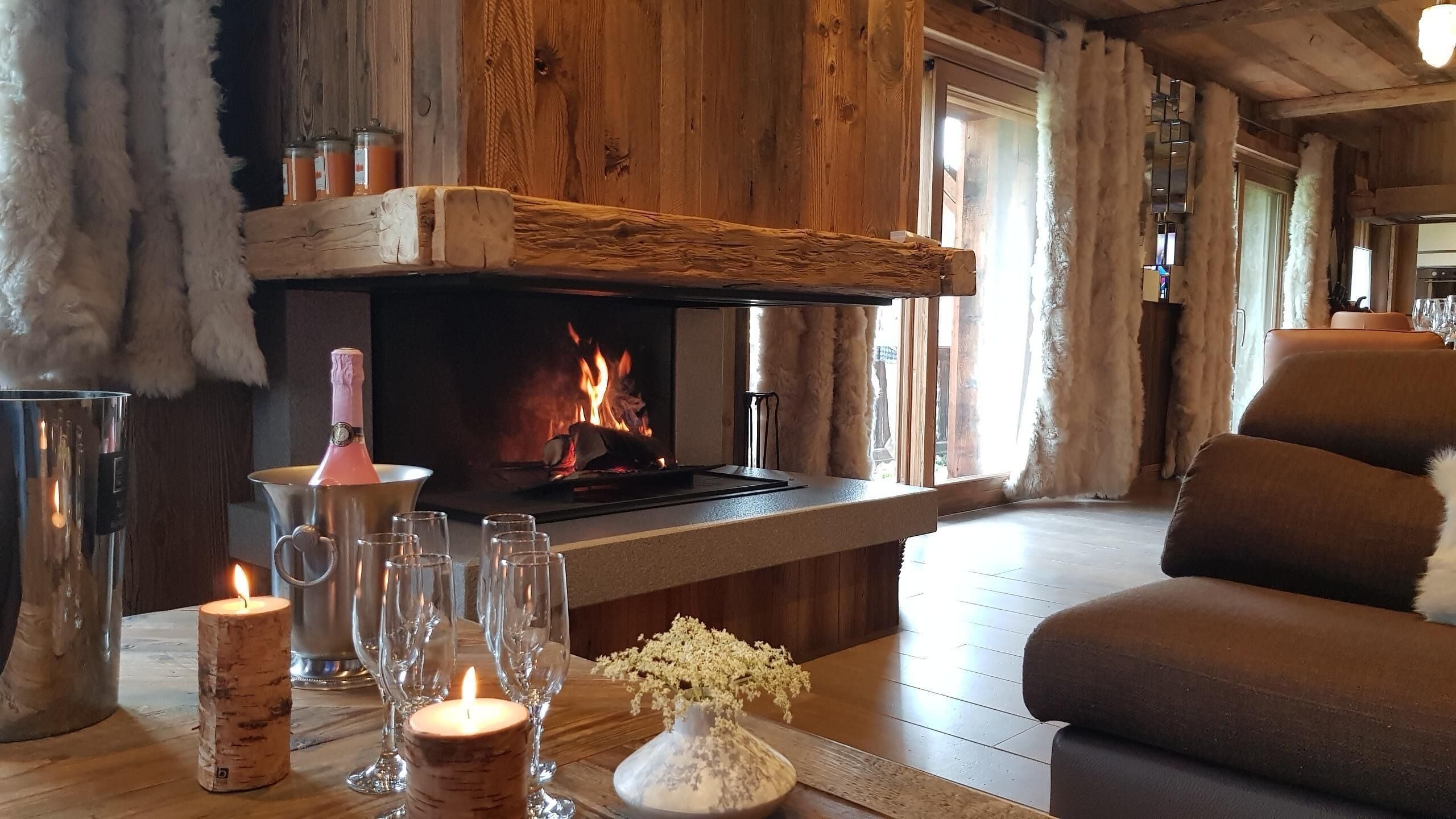 Une pièce chaleureuse avec une cheminée, un canapé et une table agrémentée de verres et de bougies.