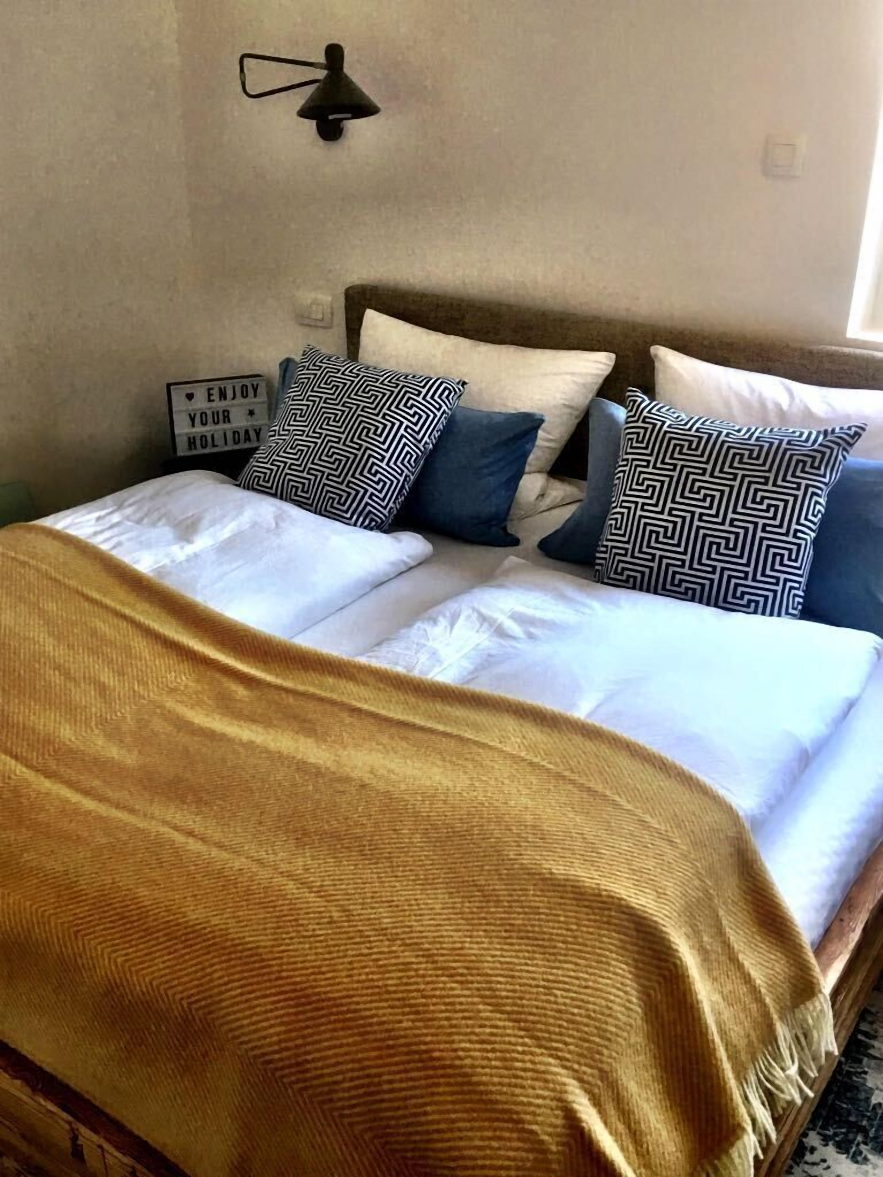 Un lit avec une couverture beige, du linge de lit blanc et des coussins à motifs.
