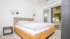 Een moderne slaapkamer met een houten bed, witte beddengoed, een klein nachtkastje en een groot raam met uitzicht op palmbomen.