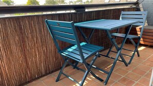 Een terras met een blauwe metalen tafel en stoelen, een bamboe hek en een betegelde vloer.