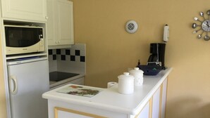 A compact kitchen with white cabinets, a microwave, a stove, a coffee maker, and a clock on the wall. - House 2 bedrooms Pierre et Vacances Port Bourgenay Domaine du Moulin (Talmont -Saint-Hilaire)