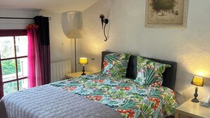 A bedroom with a bed, two bedside lamps, a window with curtains, a wall-mounted lamp, and a framed botanical print. - House "Ciboulette (Mirabel-aux-Baronnies)