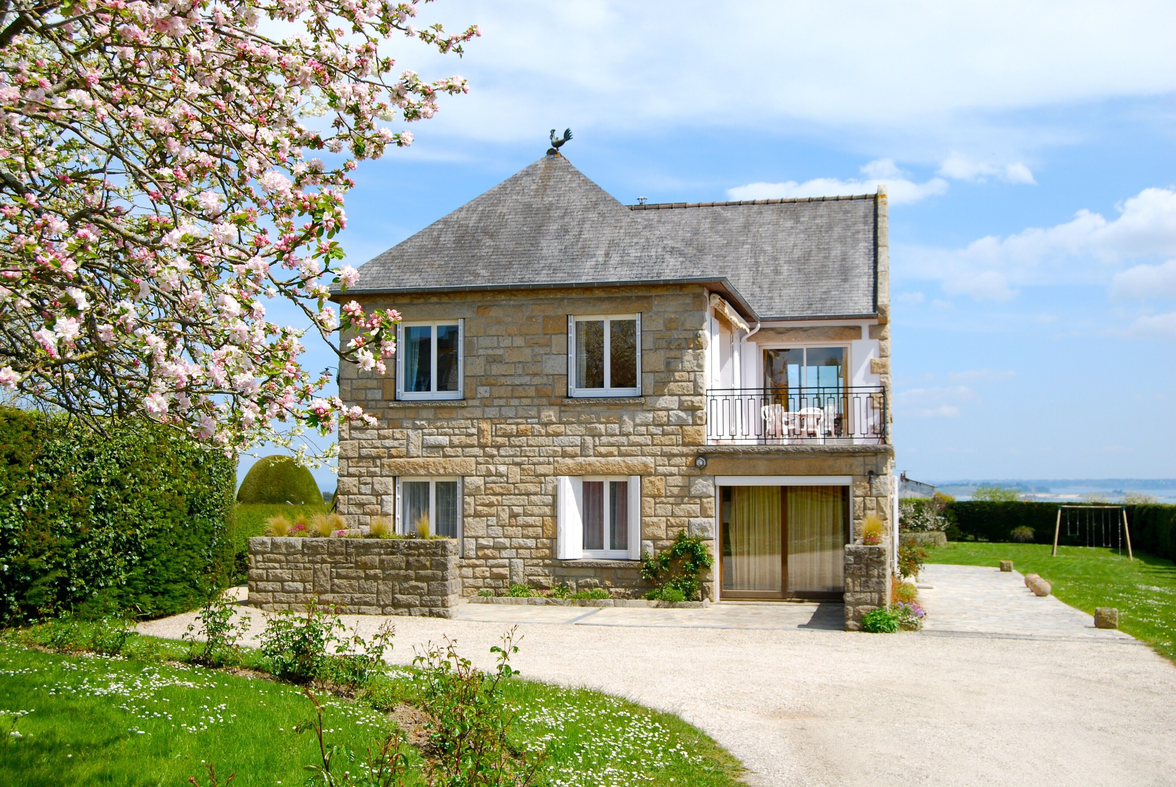 A two-story stone house with a balcony, a garage, and a driveway leading to the entrance.