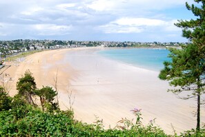 A coastal beach with a sandy shore, clear blue water, and a town in the background. - VILLA GROUND FLOOR, NEAR THE BEACH, SEA VIEW, INTERNET, BIG GARDEN (Saint-Cast-Le-Guildo)