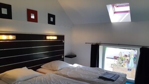 A hotel room with two beds, a skylight, a view of the outside, and a small table with a lamp.