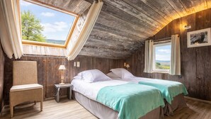 A room with two beds, a small table, a chair, and a window with a view.