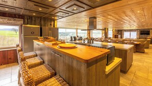 A spacious kitchen with a large island, wooden ceiling, and a view of the outdoors.