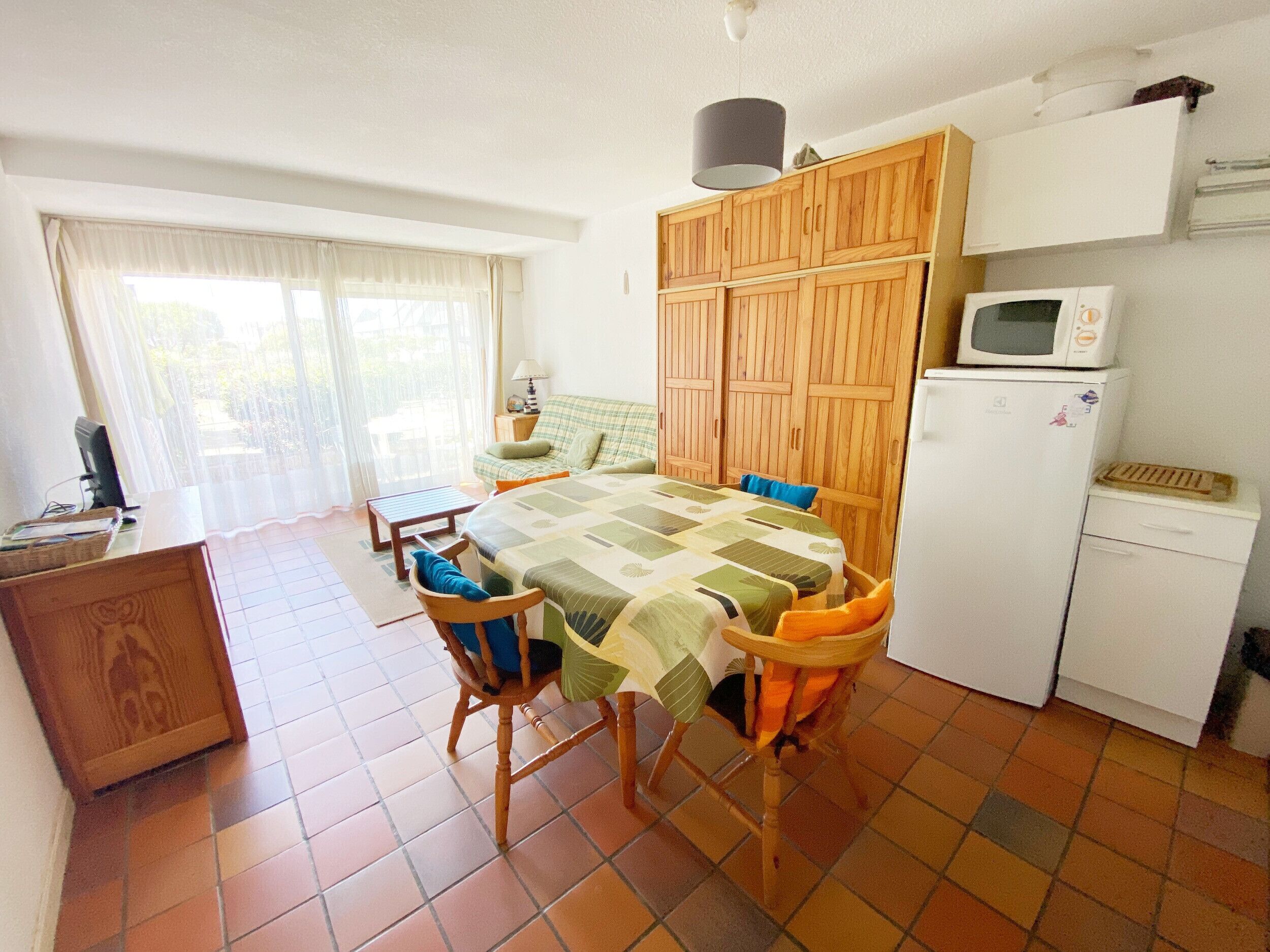 Een kleine keuken met een eettafel, stoelen, een magnetron en een koelkast.