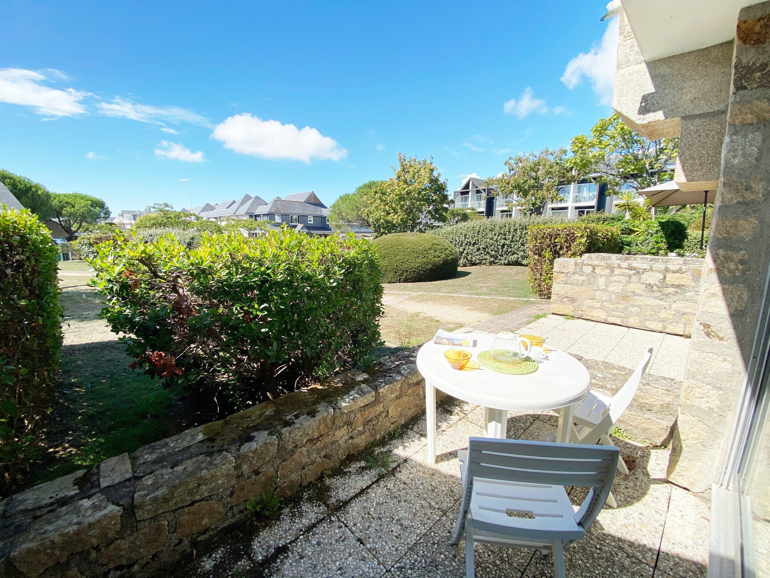 Eine Terrasse mit Tisch und Stühlen, ein kleiner Garten und eine Steinmauer.