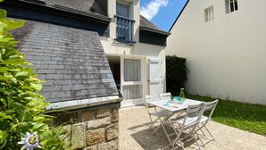 A patio with a table and chairs, a stone wall, and a house with a dark roof and white exterior. - KERNEVEST - Jardin, Tennis, Plage 600m - DT185 (Saint-Philibert)