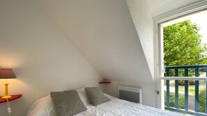 A bedroom with a bed, a lamp, a radiator, and a window with a view of greenery. - KERNEVEST - Jardin, Tennis, Plage 600m - DT185 (Saint-Philibert)