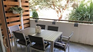 A patio with a table and chairs, a hanging plant, and a view of greenery.