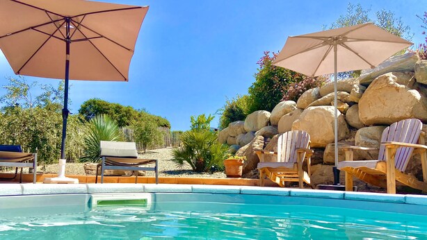 Une piscine entourée de rochers et de verdure, avec des chaises longues et des parasols.