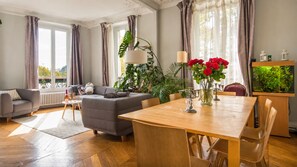 Ein modernes Wohnzimmer mit einem grauen Sofa, einem Holzesstisch und einem großen Fenster mit Vorhängen.
