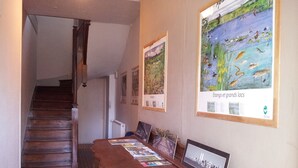 Un couloir avec un escalier en bois, un bureau en bois sur lequel sont posées des brochures, et deux affiches encadrées accrochées au mur.