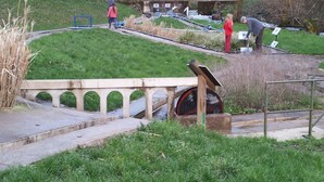 Un parc avec un pont, un élément décoratif aquatique et un petit bâtiment.