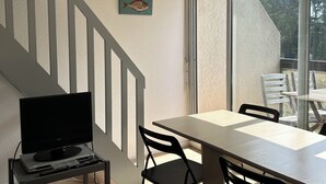 Ein modernes Zimmer mit einem Fernseher auf einem Wagen, einem Esstisch mit Stühlen und einer Treppe.