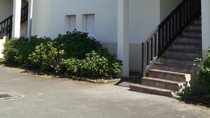 Ein mehrgeschossiges Gebäude mit flachem Dach, einer Treppe zum Eingang und einer kleinen Grünfläche davor.