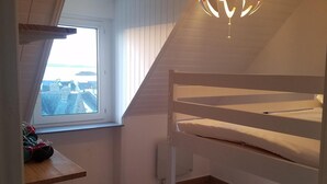 Una habitación con una cama litera, una ventana con vistas, una lámpara en el techo y una mesita con un tapete rojo.
